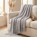 Light grey chunky knit throw blanket with fringe draped on a sofa