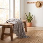 Light grey chunky knit throw blanket with fringe on a wooden bench