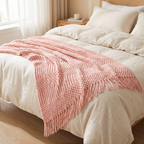 Pink chunky knit throw blanket with fringe on a bed