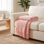 Pink chunky knit throw blanket with fringe on a sofa