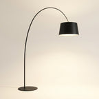 Nordic minimalist arc floor lamp in matte black with a single curved arm, inverted-cone shade and thin round disc base, glowing warm white