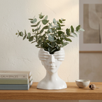 White ceramic face vase with eucalyptus sprigs styled on an open wooden shelf