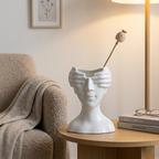 White ceramic face vase with a single dried stem on a side table in a reading nook