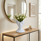 White ceramic face vase holding white tulips on an entryway console below a mirror