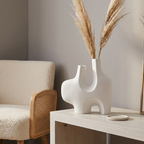 White Abstract ceramic vase with a two-prong sculptural silhouette holding pampas on a light-wood console