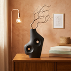 Black Abstract ceramic vase with two round cutouts holding a dried branch on a walnut sideboard