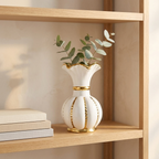 White and gold ceramic vase with eucalyptus sprigs styled on an open wooden shelf