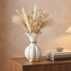 White and gold ceramic vase holding dried pampas grasses on a wooden dining sideboard
