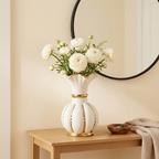 White and gold ceramic vase holding white ranunculus on an entryway console below a mirror