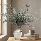 Faux olive branch in a tall glass vase against a warm plaster wall