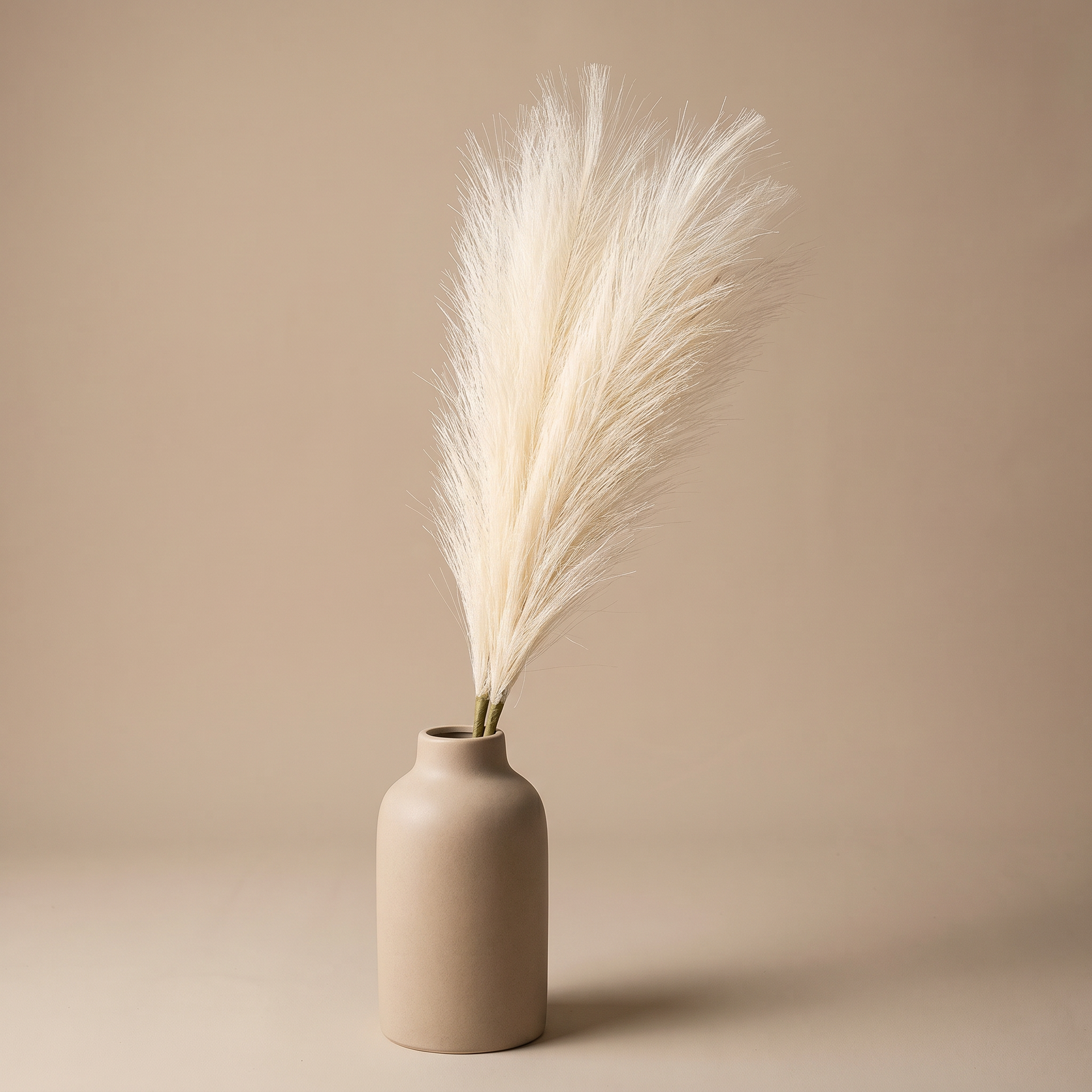 Faux pampas grass stems arranged in a tall ceramic vase on a console table