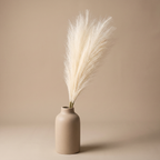 Faux pampas grass stems arranged in a tall ceramic vase on a console table
