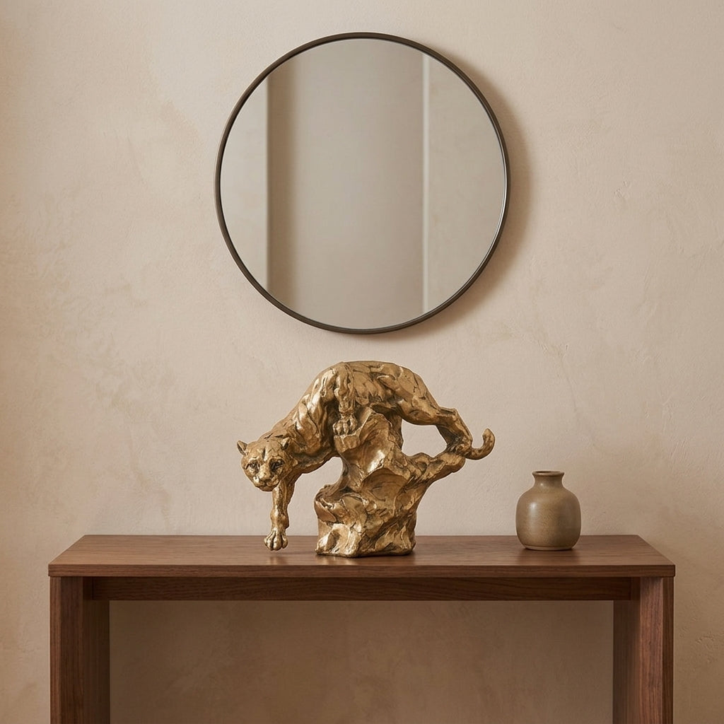 Antique-gold panther resin sculpture in a descending pose on an entryway console table with a round mirror