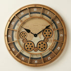 Golden world-map gear wall clock with exposed brass-toned gears, golden metal frame and minute-track numerals, front view on a warm-white studio background
