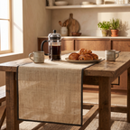 Natural linen runner with a dark contrast-bound edge on a reclaimed-wood breakfast table with a French press and croissants