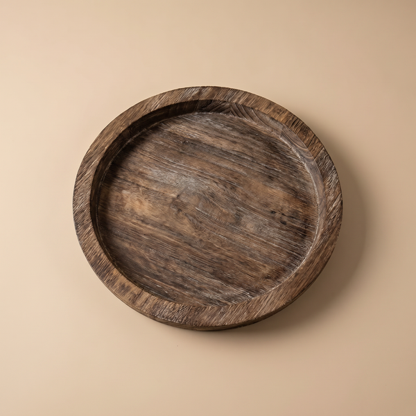 Round natural wood tray holding a pillar candle on a console table