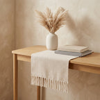 Cream waffle-weave cotton table runner with tassel fringe on a slim wooden console table