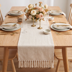 Cream waffle-weave cotton table runner with hand-knotted tassel fringe on a set dinner table with a floral centerpiece