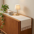 Cream waffle-weave cotton table runner with tassel fringe on a wooden sideboard