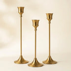 Set of three vintage tapered metal candle holders in graduated heights — on warm cream studio backdrop