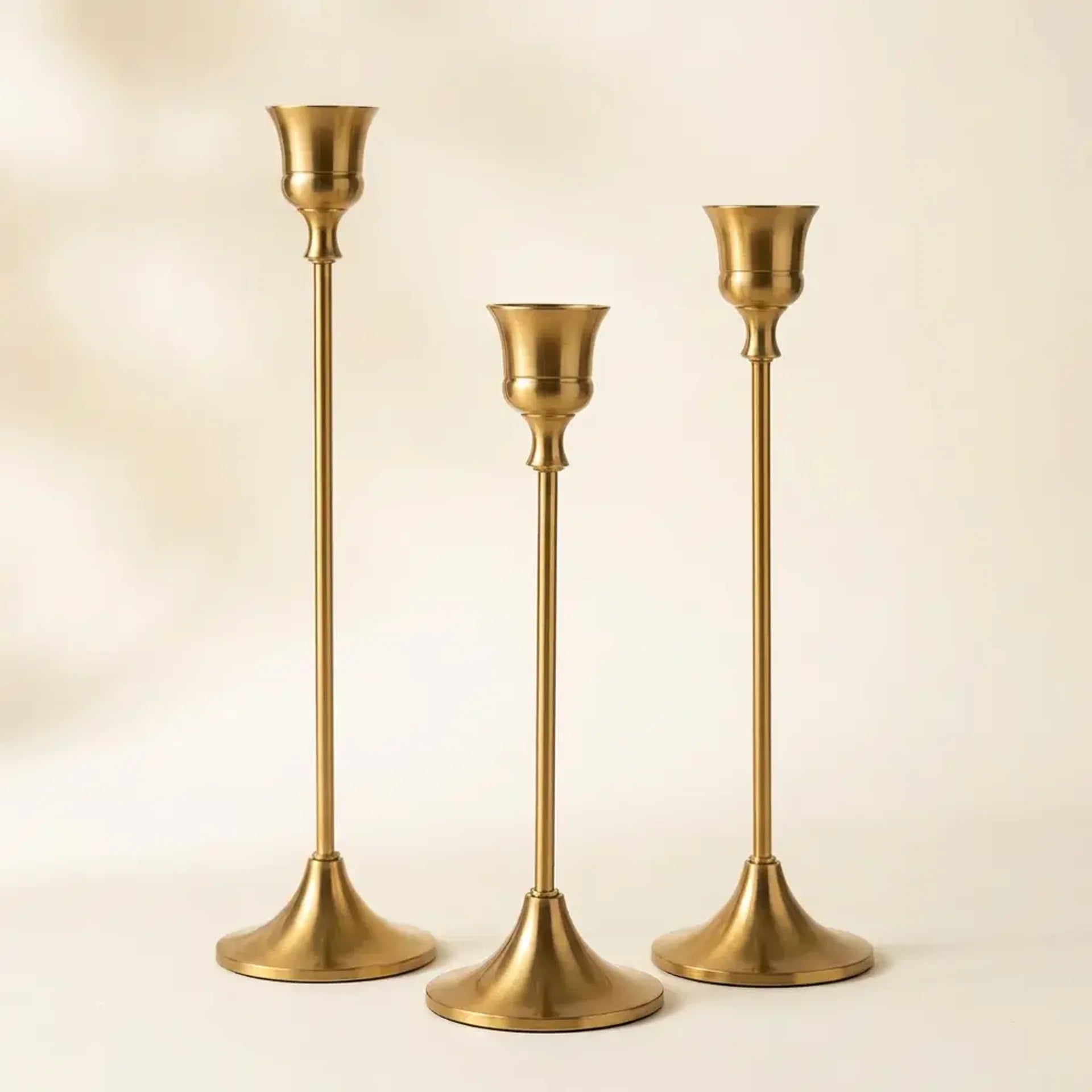 Set of three vintage tapered metal candle holders in graduated heights — on warm cream studio backdrop