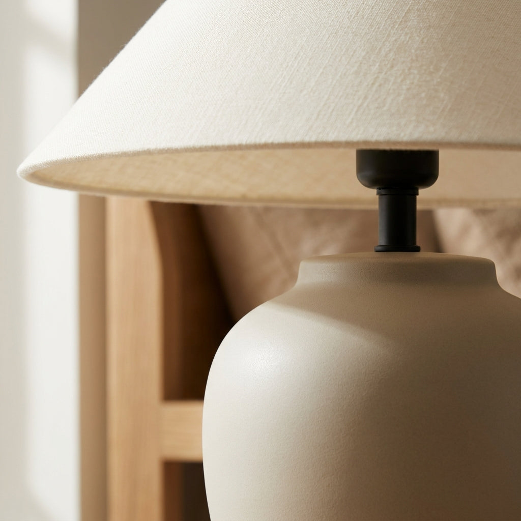 Cream coolie fabric shade of the wabi-sabi ceramic-look lamp diffusing a soft warm glow.