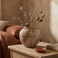 Round rustic wabi-sabi ceramic pot vase with dried stems on a bedroom nightstand