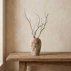 Tall rustic wabi-sabi ceramic urn vase holding dried branches as a tabletop piece on a wooden console table