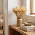 Tall dried wheat bundle beside neutral books and a stoneware bowl on an open shelf